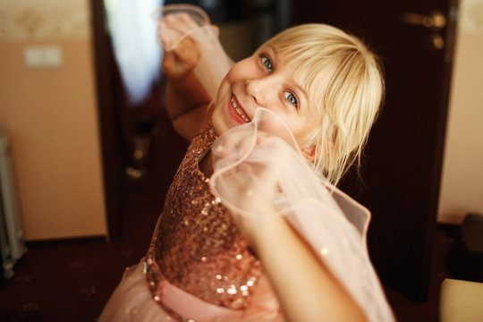 Funny little girl in sparkling pink dress has fun posing in the room