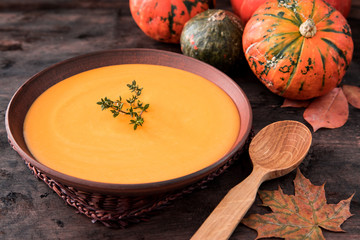 Pumpkin puree soup with thyme on a dark wooden background.