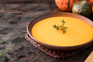Pumpkin puree soup with thyme on a dark wooden background.