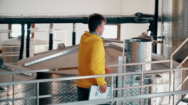 Man employee working at wine factory on background storage tanks