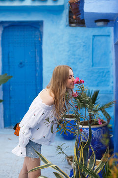 Woman smells a pink flower standing on a blue street somewhere in Morocco