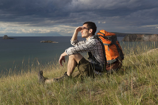 young tourist man with a backpack on the lake, Lake Baikal,  summer tourist walk, freedom and happiness