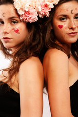 Two beautiful women with brunette hair, pink flowers in their hair and paintings on the face look like twins