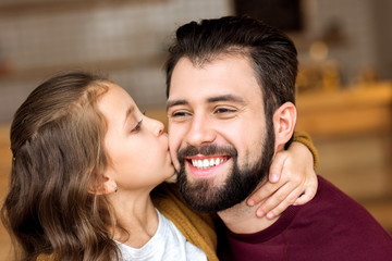 portrait of daughter kissing smiling father in cafe