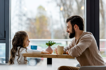 happy father and daughter sitting in cafe and looking at each other