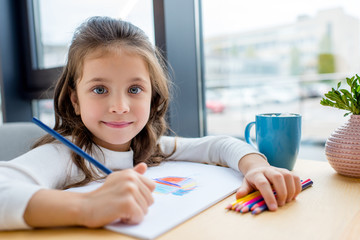 adorable kid holding colored pencil and looking at camera
