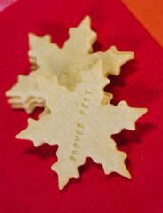 Thin, freshly baked Christmas butter sugar cookies cut out in star shape saying the German words Frohes Fest, which means Happy Holidays, on red table cloth