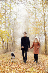 Fototapeta premium Couple walking with dog in the Park and hugging. Autumn walk men and women with a dog. Romance and love on an autumn landscape