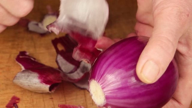 Woman peels a red onion by hands and knife