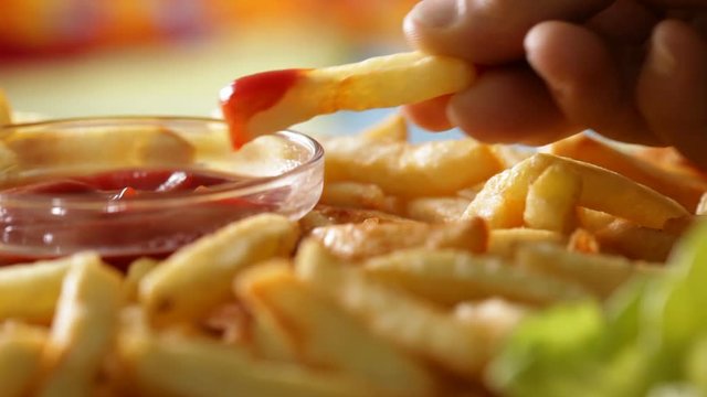 Macro closeup of eating french fries - hand taking and dipping a fried potato stick in ketchup