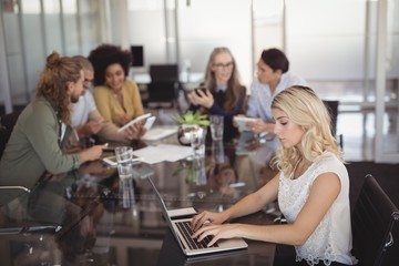 Young businesswoman using laptop on conference table with team