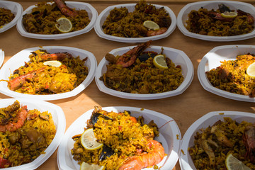 Ready paella spread out in plastic plates for distribution at a common table.