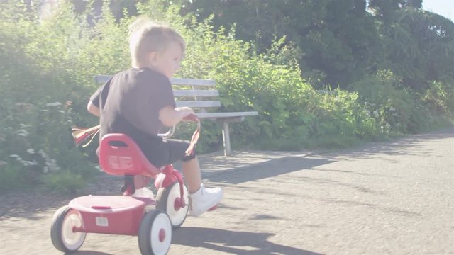 Little kid riding a tricycle on a windy day at the park. Lens flare
