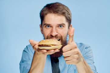 Man with a beard on a blue background holds a hamburger, fast food, portrait, emotions