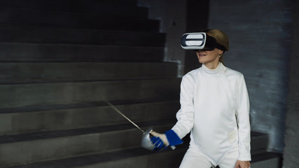 Concentrated fencer woman practice fencing exercises using VR headset and training simulator...