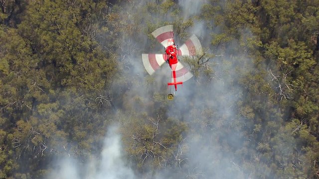 A birds eye view shot of mountains and trees with smoke and  a fire on trees. Camera zooms in to the smoke