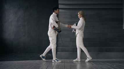 Fototapeta na wymiar Two fencers man and woman shake hands each other at the end of fencing competition indoors