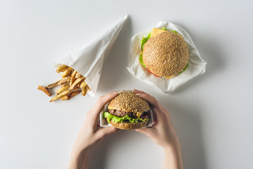 cropped view of hands with hamburgers and french fries in paper cone, isolated on white