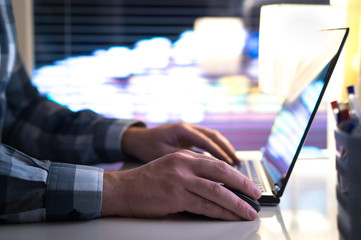 Man using laptop late at night or evening. Internet browsing or online shopping or playing games concept. Home with modern technology and city lights from the window.