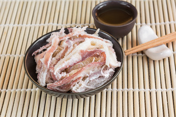 dried shredded squid in a ceramic with chopsticks and cup of tea dish on bamboo, close up.