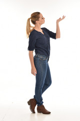 Full length portrait of a girl wearing simple blue shirt and jeans, standing pose side profile, on a white background.