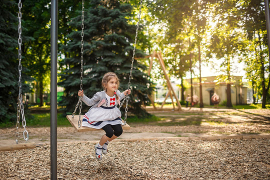 Cute little girl on a swing. Smiling child playing outdoors in summer.