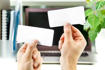 Communication at work, business interaction, learning new foreign language in school or debate concept. Hands holding two blank speech bubbles in front of a laptop in office workstation.