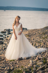 Fototapeta na wymiar Romantic beautiful bride in white dress posing on sea and mountains in background