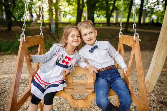 Boy and girl on a swing. Children playing outdoors in summer.
