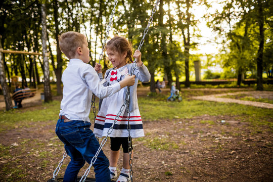 Boy and girl on a swing. Children playing outdoors in summer.