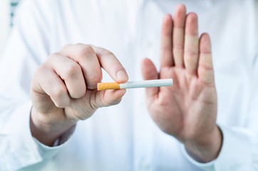 Doctor telling to quit smoking. Holding cigarette between fingers and showing stop sign with hand.
