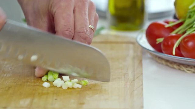 PAN with close up of hands of male professional cook chopping fresh spring onion on wooden board