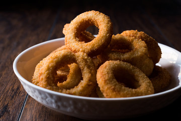 Homemade Crunchy Fried Onion Rings on dark wooden surface.