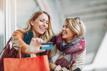 Happy friends shopping. Two beautiful young women enjoying shopping in the city holding credit card