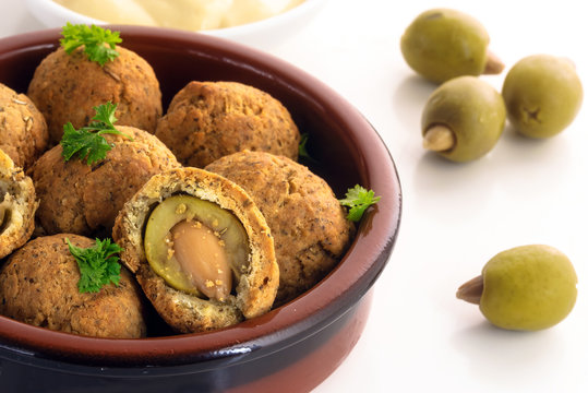 baked olives in a dough coat with parmesan cheese, party finger food, spanish tapas appetizer in a typical brown ceramic bowl on a white table, close up
