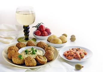 appetizers and a glass of white wine, spanish tapas such as baked olives, prawn shrimps, potatoes, tomato and garlic sauce as a corner background on white with copy space