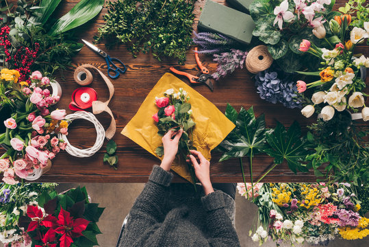 cropped image of female florist wrapping bouquet in pack paper