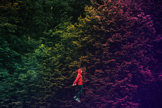 Imagen de joven con capucha roja flotando en un espejo bosque de árboles multicolores y estrellas