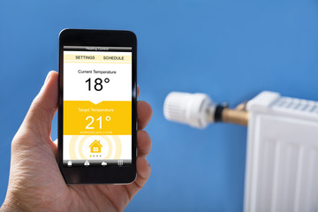 Person Hand Setting Temperature Of Thermostat Using Mobilephone