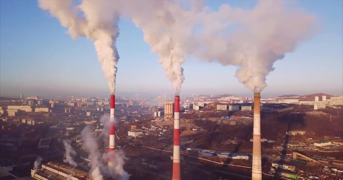 Great aerial view of three high Central Heating and Power Plant chimneys with steam rising from them. Vladivostok is on the background, Russia. Sunrise