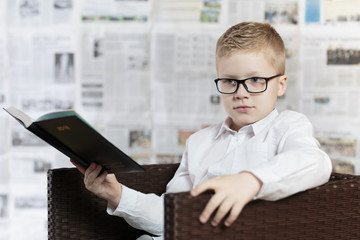 Chłopiec w okularach, czyta książkę na fotelu.