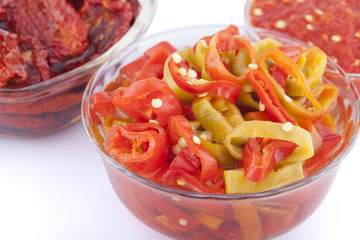 Sundried tomatoes, pieces of red and green chili pepper with oil and chili sauce in glass bowls with sackcloth cover on top isolated on white background