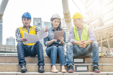 Three engineers sitting in front of building with blueprint on hand,Businessman,Engineers reading...