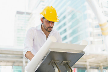 Engineer man wearing safety helmet and hold blueprint document at construction site. concept of work office, security consult, job control, development and business process.
