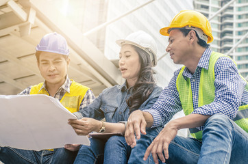 Three engineers sitting in front of building with blueprint on hand,Businessman,Engineers reading in blueprint instructions on hand in front of building