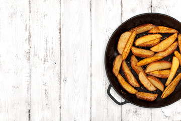 Potato wedges in a cast iron pan on light wooden background, top view
