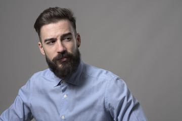 Young handsome bearded stylish confident hipster looking back over the shoulder at copyspace against gray studio background.  