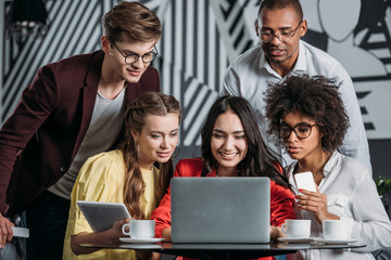 multiethnic group of happy friends lookign at laptop in cafe