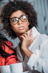 young beautiful african american woman with smartphone in hands looking away