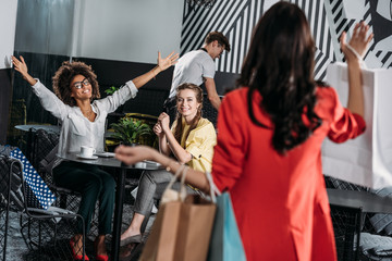 woman with shopping bags going to her friends in cafe